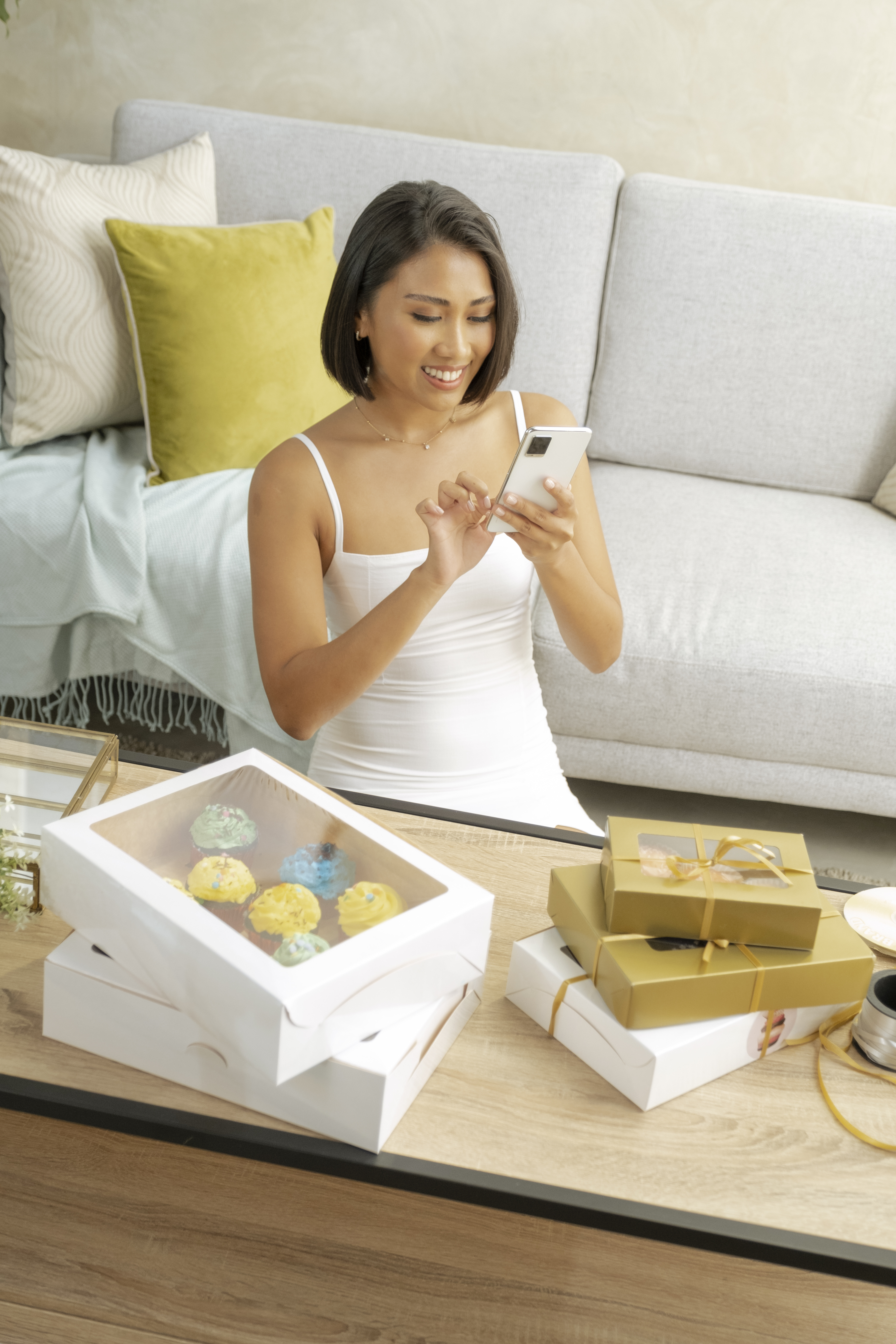 lady using phone in front of cup cake boxes